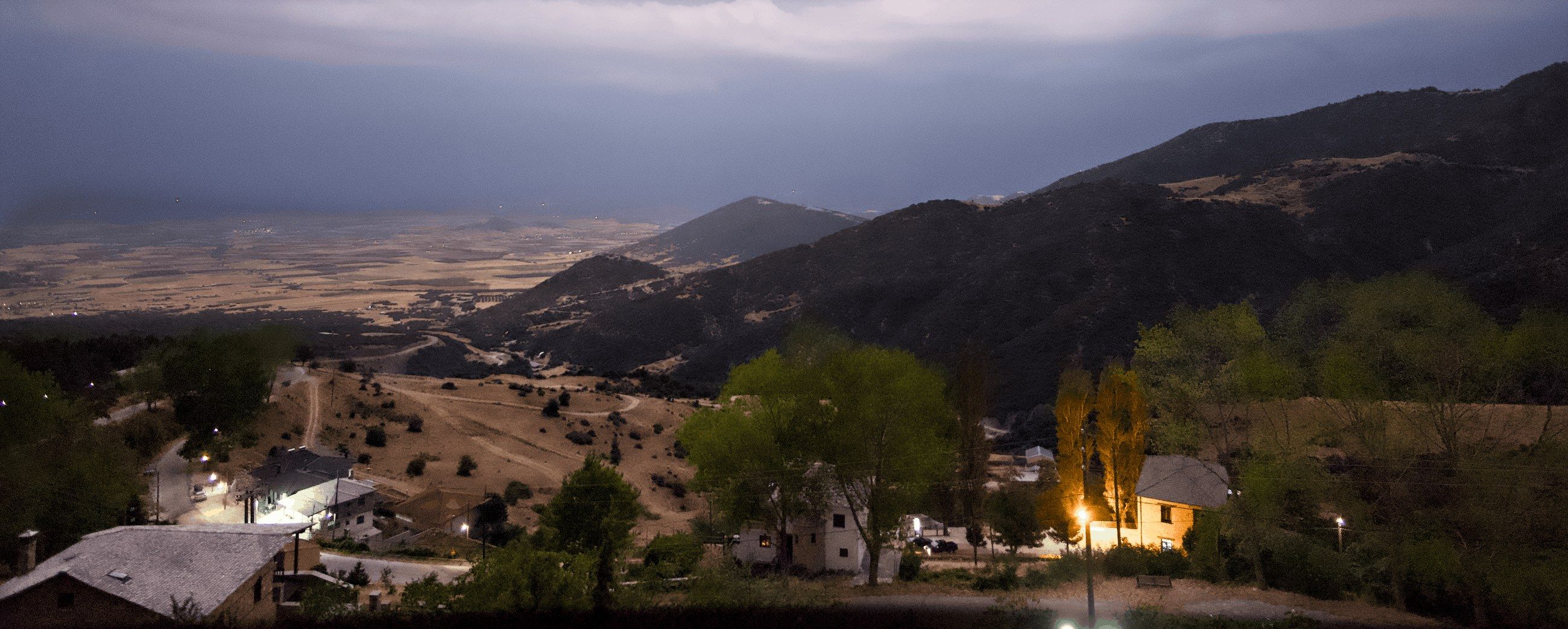 Storm clouds over the plain below Kokkinopilos at dusk, with the lights of the village in the foreground.